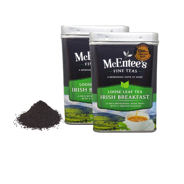 Two tins of McEntee's Loose Leaf Tea Irish Breakfast with a small pile of tea leaves on a white background.